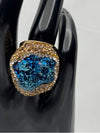 Earthy, reminiscent, bold design, oceanic blue hue center stone surrounded by textured, gold-toned settingone size fits allstatement ringvacation ring bold ringunique designgold jewelry gold ring earthy ring