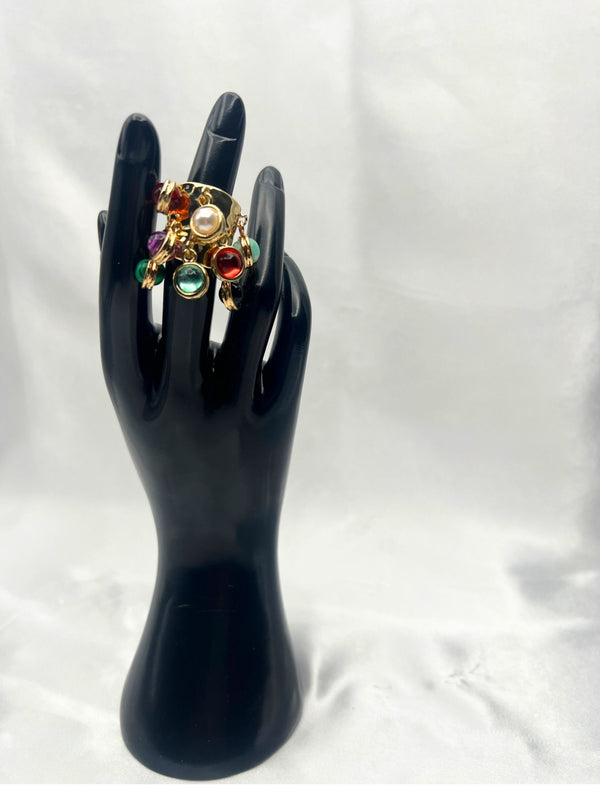 luxurious gold-tone band adorned with multiple vibrant, natural-colored stone charms. Each charm showcases a different gem, including shades of green, red, purple, black, and white with aunique dangling design. statement ringgold-tone ring with charmsmulticolor stone ringadjustable gemstone ringboho chic jewelrybold fashion ringeclectic ring designnatural stone jewelryunique tassel ringtrendy women's accessories