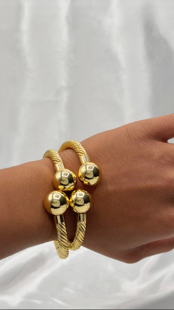 Gold bangle braceletSpherical gold braceletTwisted cable bangleLuxury fashion jewelryStatement braceletElegant gold-tone jewelryOpen-ended bangleGlamorous wrist accessoryModern chic braceletPolished gold spheresAdjustable gold bangleBold statement jewelryTimeless gold bracelet designWomen’s fashion jewelryMetallic statement piece
