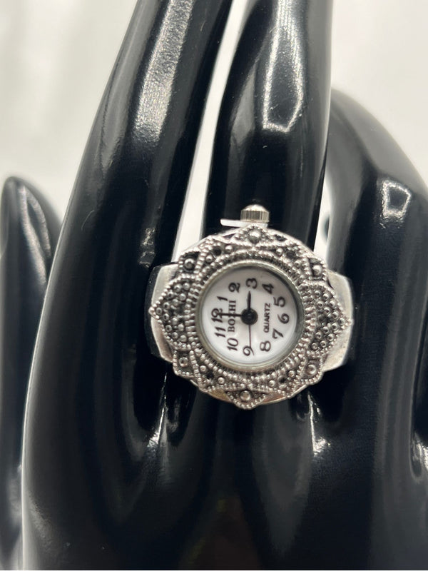 vintage-style silver-tone watch ring. Ornate bezel with intricate detailing. The round white dial with clear black numerals provides easy readability. Antique-inspired design. Perfect for vintage jewelry lovers who appreciate a statement piece with a practical twist.vintage-style watch ringsilver-tone watch ringornate bezel ring watchantique-inspired watch ringwomen’s fashion ring watchfunctional jewelry with vintage designquartz ring watch for womenstylish timepiece ringunique silver watch ring